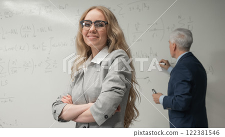 An elderly man writes on a white board and a young woman stands thoughtfully. An elderly man writes on a white board and a young woman stands thoughtfully. 122381546
