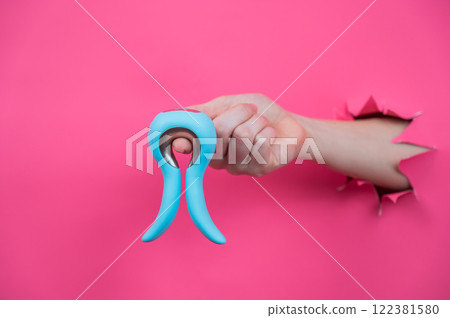 Female hand sticking out of pink paper background with blue curved vibrator sex toy.  122381580