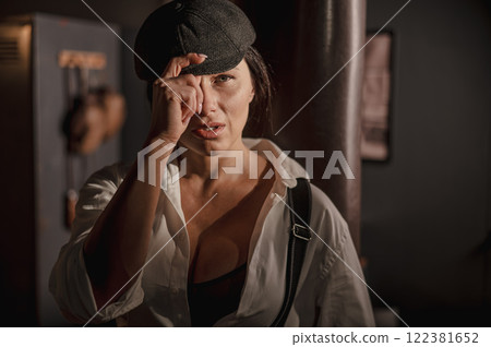 Caucasian woman in a Peaky Blinders style men's suit posing in a retro gym. Caucasian woman in a Peaky Blinders style men's suit posing in a retro gym. 122381652