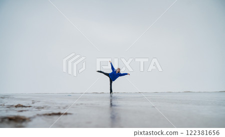 Caucasian woman in a blue sweater is skating on a frozen lake. Figure skater performs a swallow.  122381656