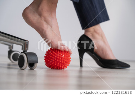Business woman massages her feet on a massage ball with spikes. 122381658