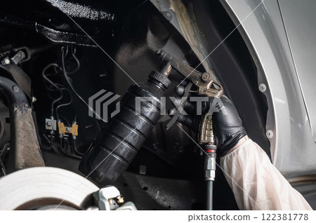 An auto mechanic applies anti-corrosion mastic to the underbody of a car. An auto mechanic applies anti-corrosion mastic to the underbody of a car. 122381778