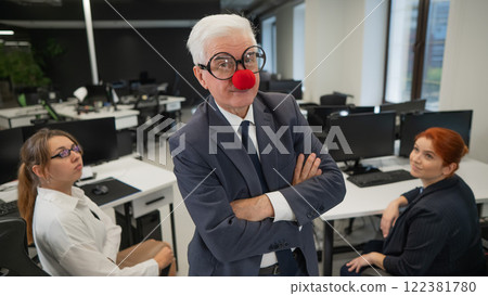 An elderly man in a clown costume fools around at work. 122381780