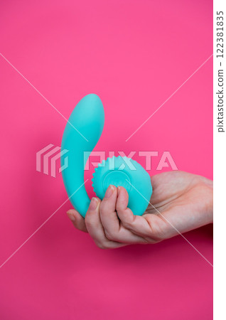 Hand with blue vibrator sticking out through pink paper background. Vertical photo.  122381835