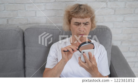 Elderly Caucasian woman with myopia and trying to read a message on a smartphone using a magnifying glass. Elderly Caucasian woman with myopia and trying to read a message on a smartphone using a magnifying glass. 122381852