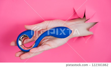 Hand with blue vibrator sticking out through pink paper background. Hand with blue vibrator sticking out through pink paper background. 122381862