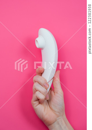 Woman holding white vacuum clitoral vibrator on pink background.  122381938