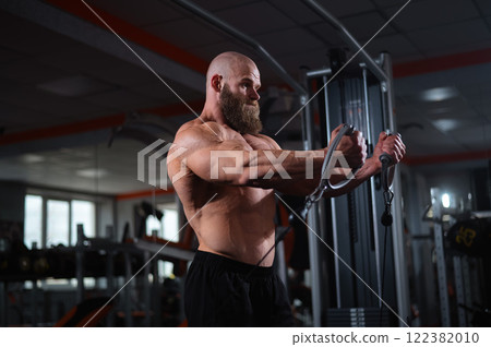 Bald Caucasian bodybuilder training chest using cable crossover in gym. Bald Caucasian bodybuilder training chest using cable crossover in gym. 122382010