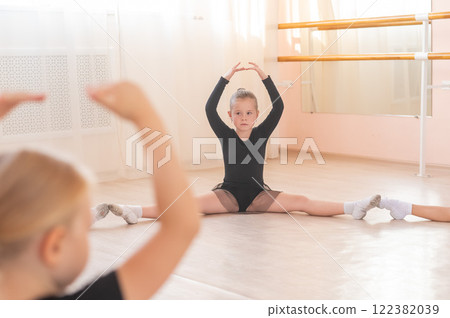 Little girls sit in a circle and do stretching at a ballet school. Little girls sit in a circle and do stretching at a ballet school. 122382039