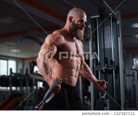 Bald Caucasian bodybuilder training chest using cable crossover in gym.  122382112