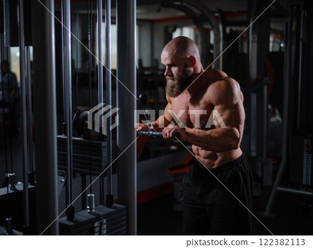 Bald Caucasian Bodybuilder doing heavy triceps exercises with cable. Bald Caucasian Bodybuilder doing heavy triceps exercises with cable. 122382113