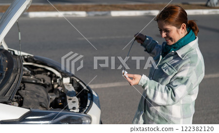 Caucasian female driver checking oil level in car engine.  122382120