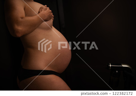 Close-up of the belly of a pregnant woman undergoing an instant tanning procedure. The master applies bronzer with a spray. 122382172