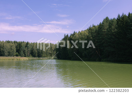 Picturesque view of a forest lake with clear water reflecting green trees and blue sky. The shore is covered with dense coniferous and deciduous trees. Film photography effect and grunge effect Picturesque view of a forest lake with clear water reflecting green trees and blue sky. The shore is covered with dense coniferous and deciduous trees. Film photography effect and grunge effect 122382203