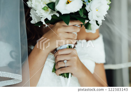 A beautiful bride holds a wedding bouquet and covers him with her face 122383143