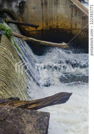 Powerful waterfall rushing over a dam with logs and moss-covered concrete. High quality photo Powerful waterfall rushing over a dam with logs and moss-covered concrete. High quality photo 122383771