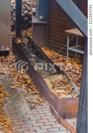 rusty metal barbecue grill sits outdoors on a patio covered in autumn leaves. High quality photo 122383781