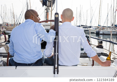 Two men in blue shirts sitting with their backs on yacht in the port Two men in blue shirts sitting with their backs on yacht in the port 122384189