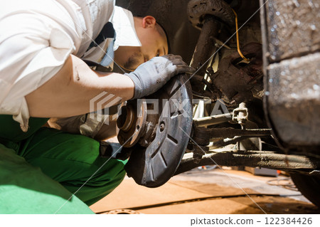 Mechanic Working on a Car's Brake System in a Garage 122384426