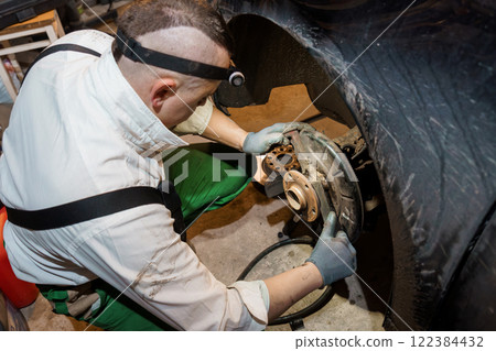 Mechanic Performing Brake Repair Underneath Vehicle in Garage 122384432