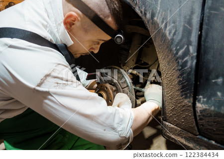 Mechanic Performing Brake Repair on a Vehicle in a Dimly Lit Garage 122384434