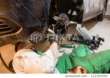 Mechanic Performing Brake Repair Under Car in Auto Shop 122384449
