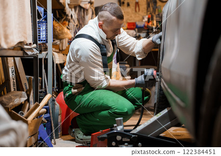 A Mechanic Working on a Car Tire in a Garage 122384451