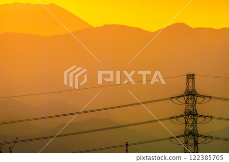 Tokyo cityscape in Japan. Sky is dyed orange... View of power towers and transmission lines. Mount Fuji in the background on the left. January 28, 2025. 122385705