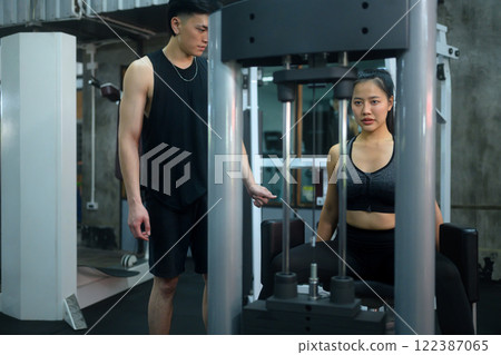 Female athlete exercising on a leg press machine under the supervision of her trainer Female athlete exercising on a leg press machine under the supervision of her trainer 122387065
