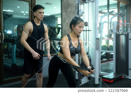 Male fitness trainer supervising a female athlete doing exercises with crossover cable in the gym 122387066