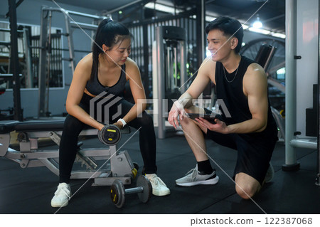 Personal trainer reviewing workout plans with a client during a break in strength training 122387068