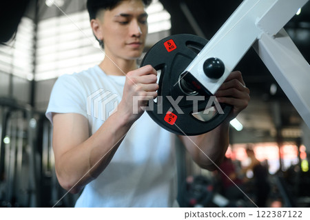Handsome man adjusting weight plate on a gym machine, preparing for a workout Handsome man adjusting weight plate on a gym machine, preparing for a workout 122387122