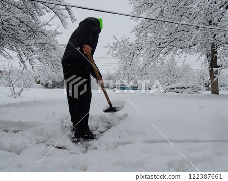 A man removes snowdrifts with a shovel, clears the path from the house to the road after bad weather, clears the adjacent territory and the driveway from snow after a snowstorm 122387661