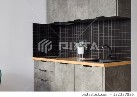 This is a modern kitchen featuring a stunning design with concrete surfaces and black tile elements This is a modern kitchen featuring a stunning design with concrete surfaces and black tile elements 122387886