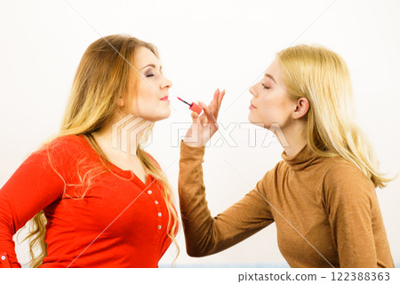 Woman applying her friend lipstick on lips Woman applying her friend lipstick on lips 122388363