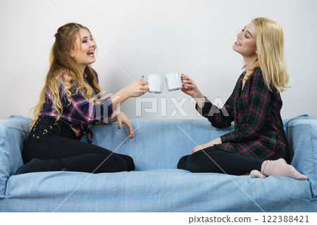 Female friends sitting on sofa having fun Female friends sitting on sofa having fun 122388421