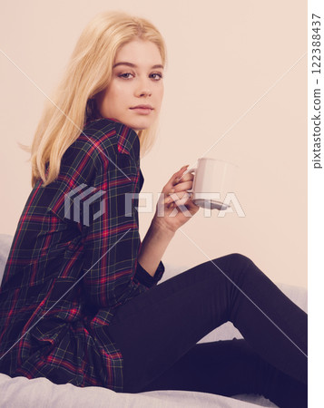 Teenage woman sitting on sofa with mug 122388437