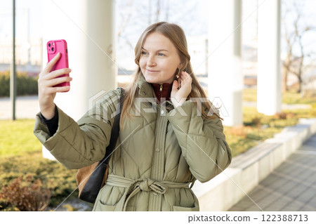 Laughing young woman taking selfie on the urban background. Cute beautiful woman using mobile phone. 30s girl recording self video, talking on online call Laughing young woman taking selfie on the urban background. Cute beautiful woman using mobile phone. 30s girl recording self video, talking on online call 122388713