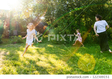 Mother and children playing and running together in a sunny backyard garden 122389151