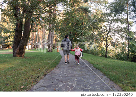 A young girl smiles brightly, holding a stuffed animal, while walking with her father in a green 122390240