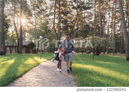 A young girl smiles brightly, holding a stuffed animal, while walking with her father in a green A young girl smiles brightly, holding a stuffed animal, while walking with her father in a green 122390241