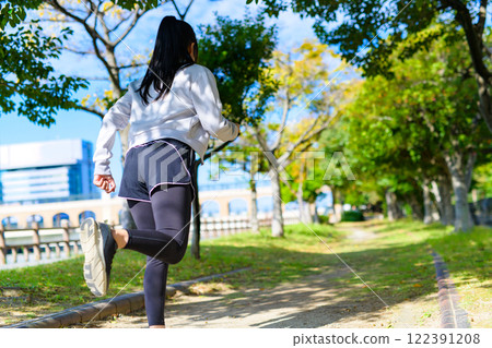 Back view of a young woman jogging along a roadside tree in an autumn park Diet Body make-up Lower body Back view of a young woman jogging along a roadside tree in an autumn park Diet Body make-up Lower body 122391208