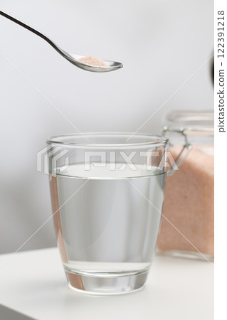 A spoon of Himalayan salt is being added to a glass of drinking water. 122391218