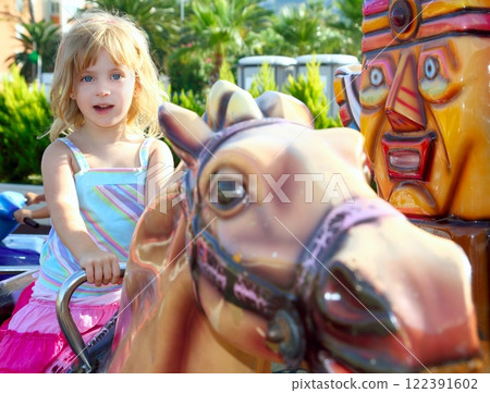 blond girl with fairground horse enjoy in park 122391602