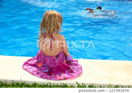 Little blond girl sitting rear back swimming pool 122391634