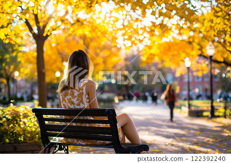 Hispanic girl sitting on a bench in a park surrounded by autumn colors during a sunny day 122392240