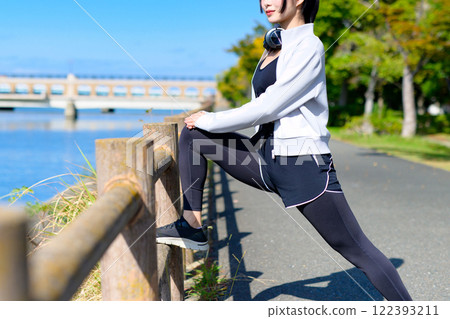 A cool woman stretching her legs on a fence along the river. Walking, dieting, walking, exercise, trimming 122393211