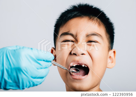 In a dental office a pediatric dentist examines a child's mouth after extraction of a loose milk tooth. Dental instruments aid in examination process. Doctor uses mouth mirror to checking teeth cavity 122393956