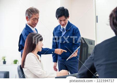 一個穿著工作服的人和一個穿著西裝的女人在辦公室談話 一個穿著工作服的人和一個穿著西裝的女人在辦公室談話 122394717