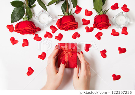 Female hands hold gift box for valentine's day. Red roses and candles on a white background. Female hands hold gift box for valentine's day. Red roses and candles on a white background. 122397236